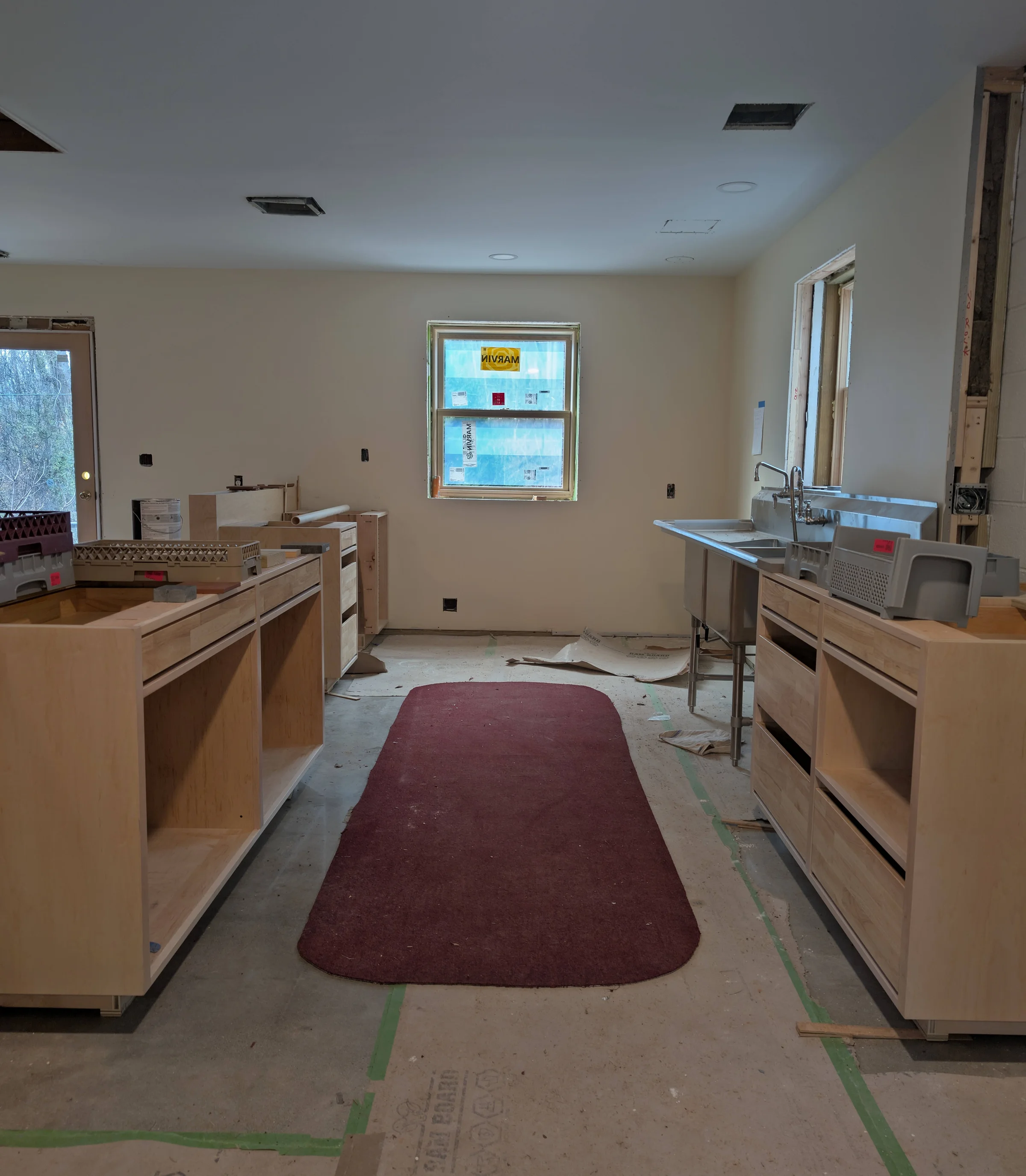 Kitchen under construction with red rug on the floor. Cabinets without drawers.