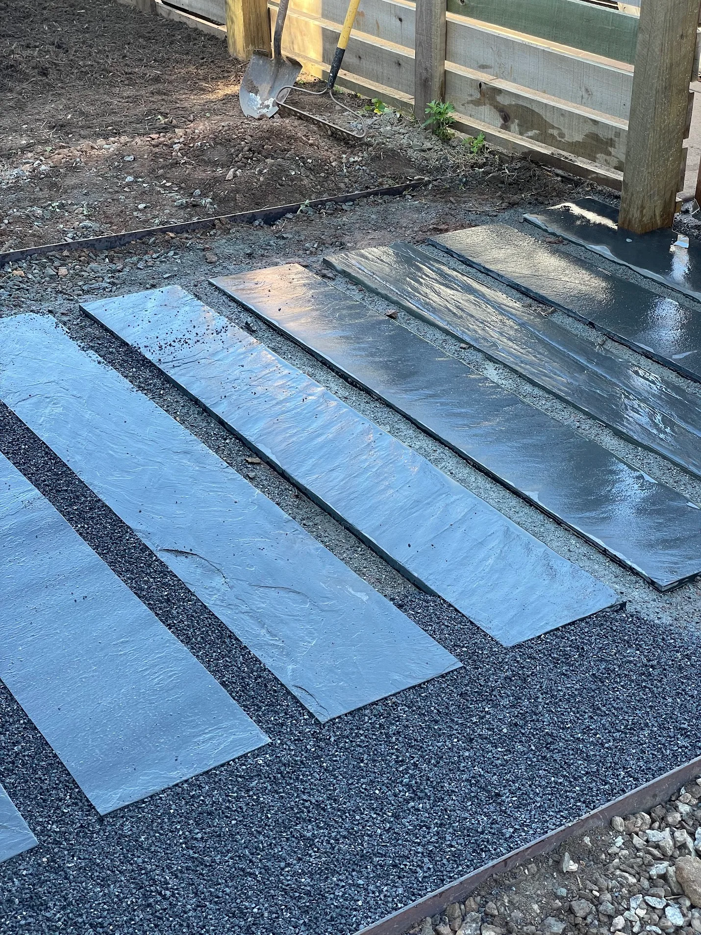 A front walkway made out of long rectangular pieces of wet slate bound by gravel.