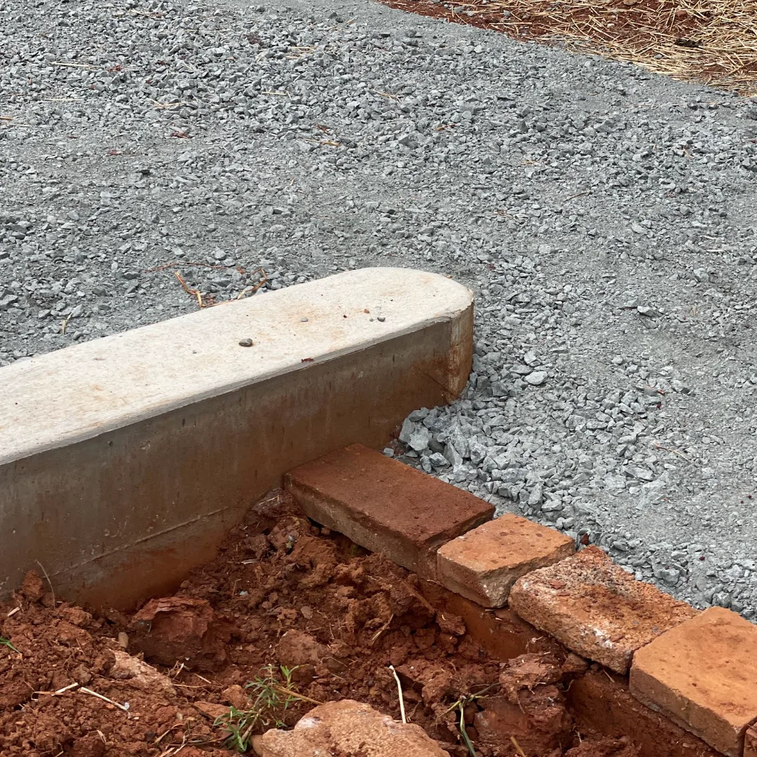 Cooncrete retaining wall with a rounded end intersects with a gravel patch and a rough rubble wall.
